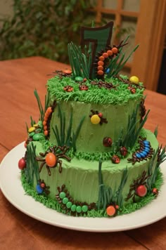 a three tiered cake with grass and bugs on the top is sitting on a table