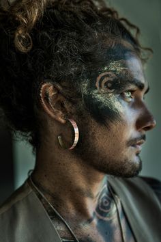 a man with his face painted black and white is looking off to the side while wearing large hoop earrings