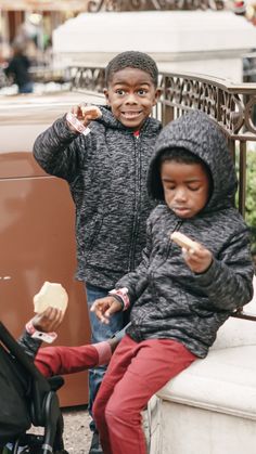 two young children sitting on a bench eating food and one is holding a stroller