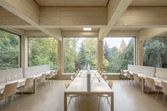 an empty room with tables and chairs in front of large windows looking out onto the woods