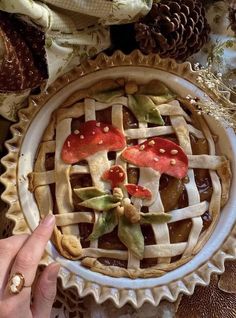 a person holding up a pie with mushrooms and leaves on it in front of some pine cones