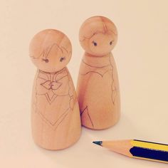 two wooden dolls sitting next to a pencil