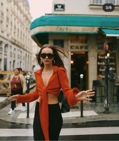 a woman in an orange sweater and black pants is walking down the street with her arms outstretched