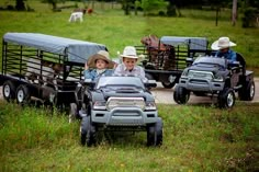 three children in toy trucks with horses and cattle on the back driving down a dirt road