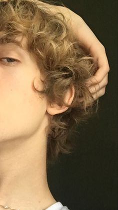 a young man with curly hair is holding his head to his ear while wearing a white shirt