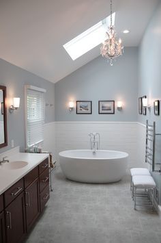 a large white bathtub sitting under a window in a bathroom next to a sink