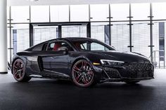 a black sports car parked in front of a building with large windows and red rims