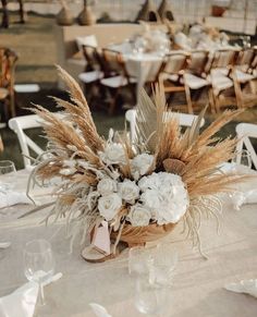 an arrangement of white flowers and wheat stalks in a basket on top of a table