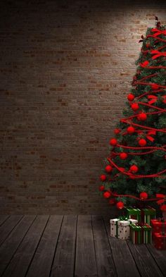 a christmas tree with presents under it on a wooden floor next to a brick wall