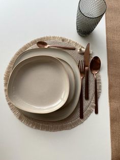 an empty plate and silverware on a white table cloth with a brown napkin next to it