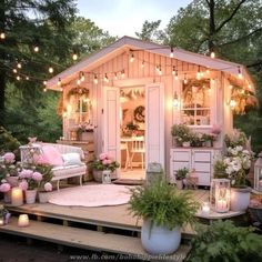 a small white shed with lights strung from it's roof and flowers on the porch