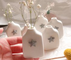 three small white vases with silver stars on them and one is holding a plant