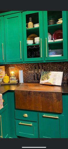 a kitchen with green cupboards and wooden counter tops in the center is an open cookbook on top of a cutting board