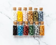 small bottles filled with different colored rocks on a marble counter top next to corks