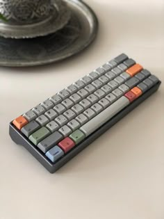 a computer keyboard sitting on top of a white table next to a silver tray with a plant in it