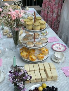 a table topped with lots of food and desserts next to pink flowers in vases