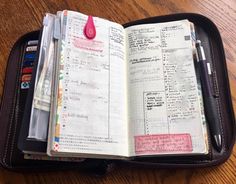 an open planner book on top of a wooden table next to a pen and calculator