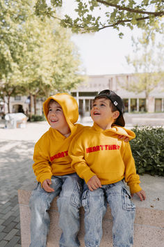 two young boys sitting next to each other on a stone bench wearing yellow sweatshirts