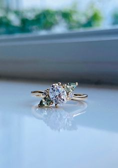 three stone ring sitting on top of a white counter next to a window sill