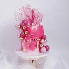 a pink and gold birthday cake sitting on top of a table