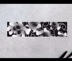 a black and white floral design on a piece of paper next to two markers with pens