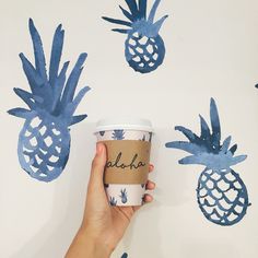 a hand holding a coffee cup with blue pineapples painted on the wall behind it