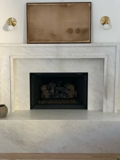 a white fireplace with a painting on the wall above it and a potted plant next to it