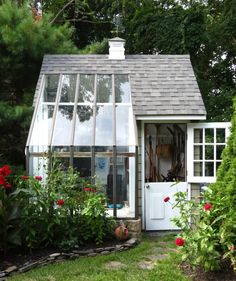 a small white house with lots of windows and flowers in the front yard, surrounded by greenery