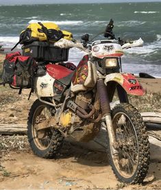 a dirt bike parked on top of a sandy beach next to the ocean and waves