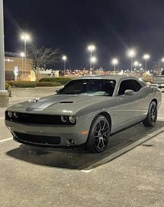 a gray car parked in a parking lot at night with the lights on behind it