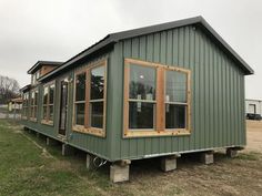 a green tiny house with windows on the front and side of it sitting in an open field