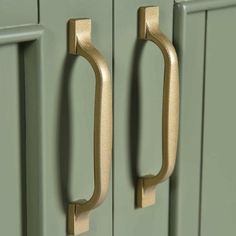 two brass handles on green cupboards in a kitchen