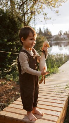 a young boy holding a stuffed animal on top of a wooden platform next to water