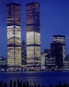 two skyscrapers are lit up at night in front of the city's skyline