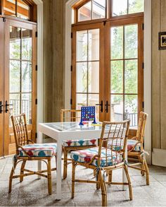 a dining room table with four chairs in front of two large windows and wooden doors