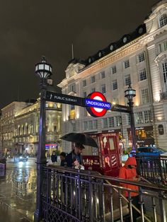 people standing under an umbrella on a rainy night in the city with buildings and street lights behind them