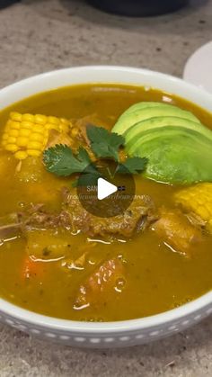 a bowl of soup with corn, avocado and cilantro on the side