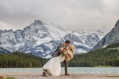 a bride and groom kissing in front of mountains