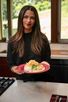 a woman holding a plate with food on it in front of a stove top oven