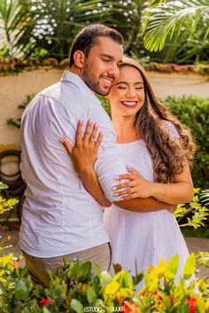 a man and woman embracing each other in front of plants