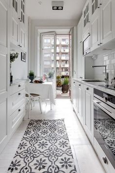 a kitchen with white cabinets and black and white rugs on the floor in front of an open door