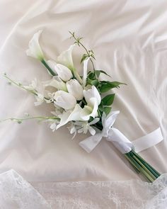 a bridal bouquet with white flowers and greenery is laying on a bed sheet