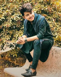 a young man sitting on top of a cement bench in front of a shrubbery