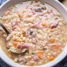 a white bowl filled with ham and bean soup on top of a blue napkin next to a spoon