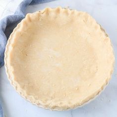 an uncooked pie crust sitting on top of a white countertop next to a blue towel