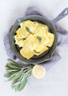 an iron skillet with some food in it and lemon wedges on the side