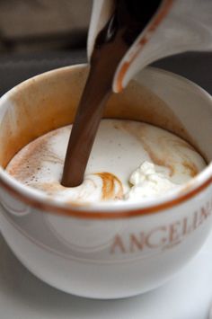 a person pouring something into a cup on top of a white saucer with an orange rim