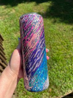 a hand holding up a purple, blue and pink tumbler cup in the grass