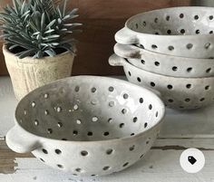 three white ceramic bowls with holes on them next to a potted succulent