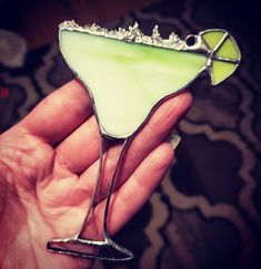 a hand holding a green and white drink in it's left hand, with the top half partially covered by silver flakes